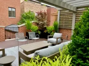 Modern Chicago Backyard patio with outdoor lounge seating, wood-look decking, integrated planters, privacy screens, and lush greenery surrounded by brick buildings.