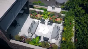 Aerial view of a Chicago rooftop deck with gray sectional sofas, a round white coffee table, woven chairs, and lush planters along a brick parapet.