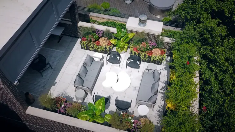 Aerial view of a Chicago rooftop deck with gray sectional sofas, a round white coffee table, woven chairs, and lush planters along a brick parapet.